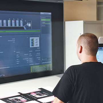 Großer Bildschirm von Offsetdruckmaschine, Mensch steht davor und bedient die Technik, Druckerei Hamburg