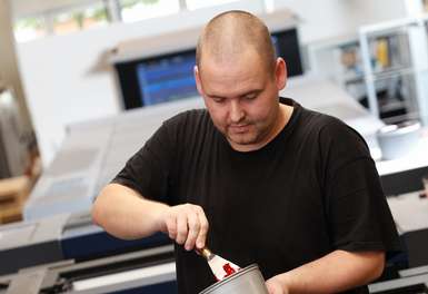 Person auf Druckmaschine vor Farbkasten mit Farbtopf und Spachtel in der Hand - Offsetdruckerei - Hamburg