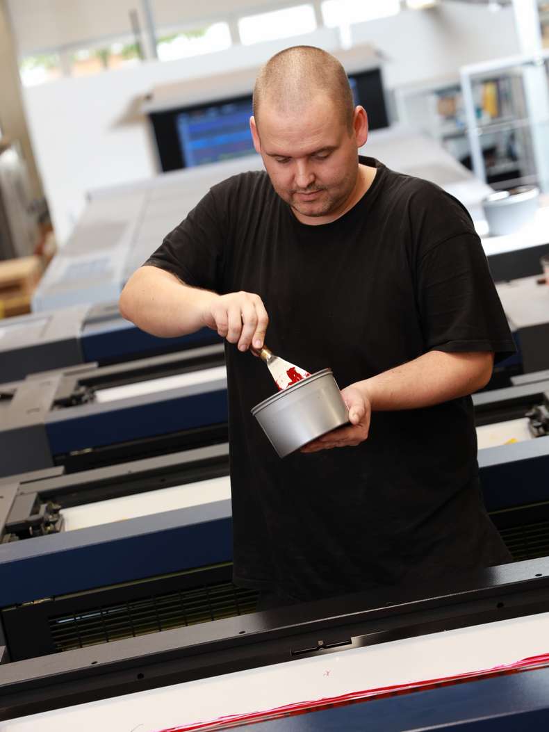 Person auf Druckmaschine vor Farbkasten mit Farbtopf und Spachtel in der Hand - Offsetdruckerei - Hamburg