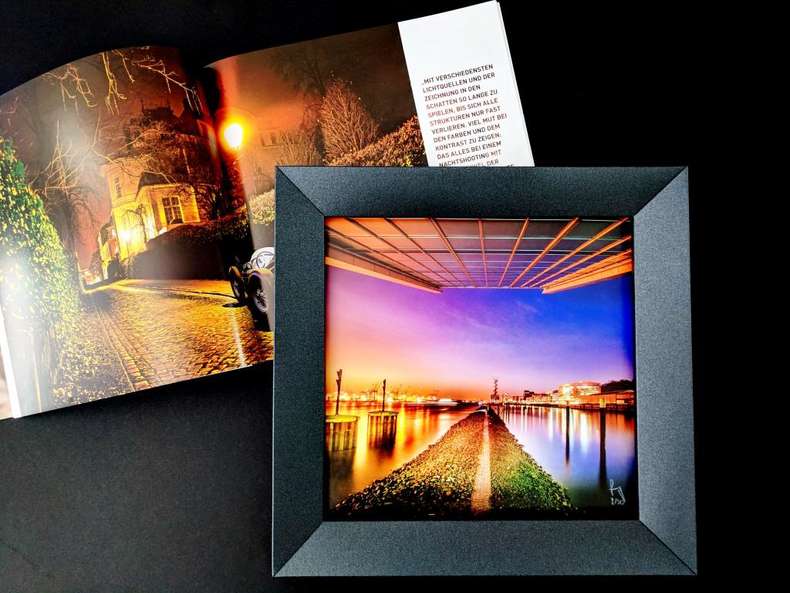 Sechsfarbdruck - PSO-Coated v3 Schwarzer Bilderrahmen mit Bild, dahinter geöffnete Broschüre auf schwarzem Hintergrund-PSO-Coated v3